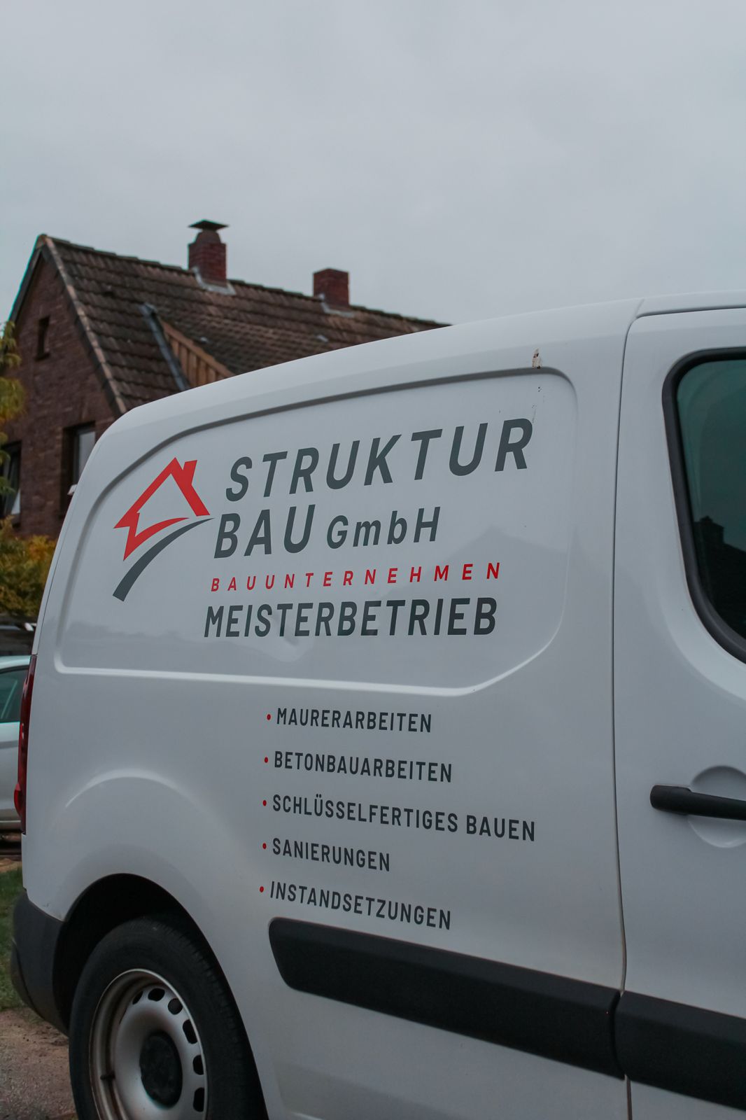 Strukturbau GmbH Oldenburg Ein weißer Lieferwagen mit dem Logo und den Dienstleistungen der STRUKTURBAU GmbH, einem Oldenburger Bauunternehmen, ist zu sehen und listet Bauangebote wie Maurer-, Betonarbeiten, Renovierung und Reparaturen in deutscher Sprache auf.