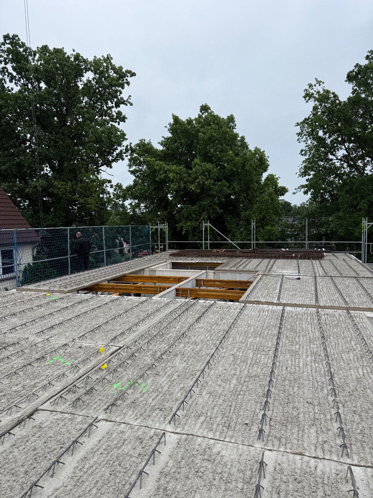 Strukturbau GmbH Oldenburg Ein im Bau befindliches flaches Betondach mit Bewehrungsstäben aus Metall und einer großen rechteckigen Öffnung in der Mitte; im Hintergrund sind Bäume und Gerüste zu sehen.
